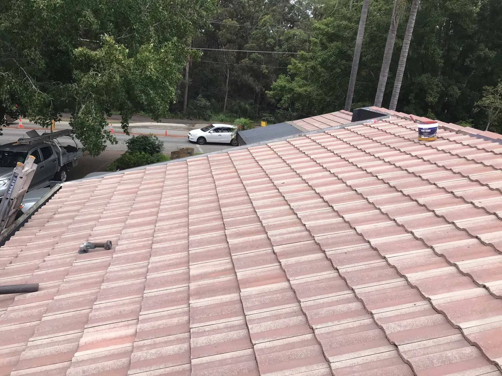 A tile roof part way through restoration on the South Coast, with the work ute and ladder in the street below